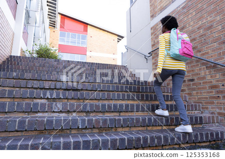 Walking up stairs, african american girl with backpack heading to school building 125353168