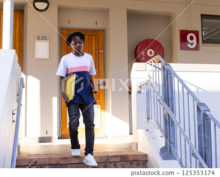 Holding folder, african american boy wearing glasses walking down stairs outside school building 125353174