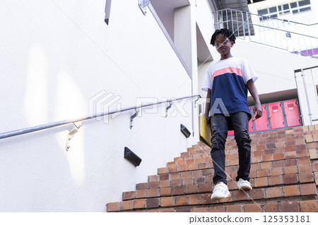 Walking down stairs, african american boy in casual clothes at school, looking confident Walking down stairs, african american boy in casual clothes at school, looking confident 125353181