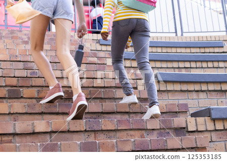 Walking up stairs, diverse girls carrying backpacks and water bottle at school 125353185