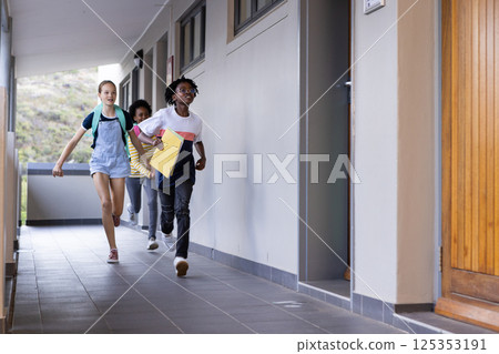 Running in school hallway, three diverse kids with backpacks and notebooks smiling Running in school hallway, three diverse kids with backpacks and notebooks smiling 125353191