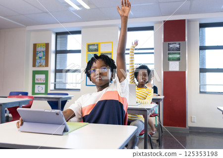 In school, diverse students raising hands while using tablet in classroom 125353198