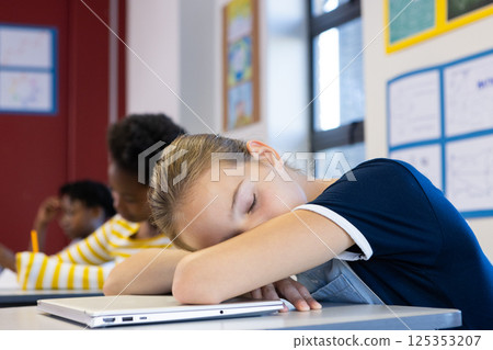 Sleeping on desk with laptop, girl in school classroom during lesson 125353207