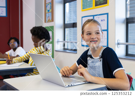 In school, girl using laptop in classroom, smiling and looking away In school, girl using laptop in classroom, smiling and looking away 125353212