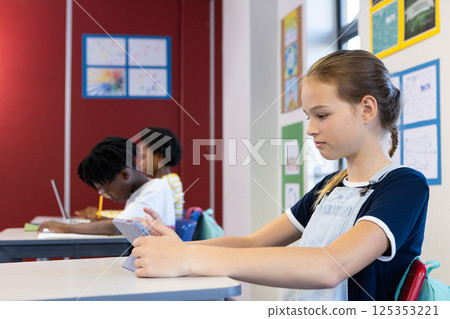 In school, girl using tablet while classmates studying at desks in classroom 125353221