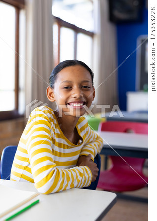 Smiling girl sitting at desk in school classroom, looking at camera Smiling girl sitting at desk in school classroom, looking at camera 125353228