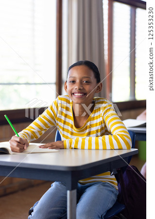 In school, girl smiling and writing in notebook at classroom desk In school, girl smiling and writing in notebook at classroom desk 125353230