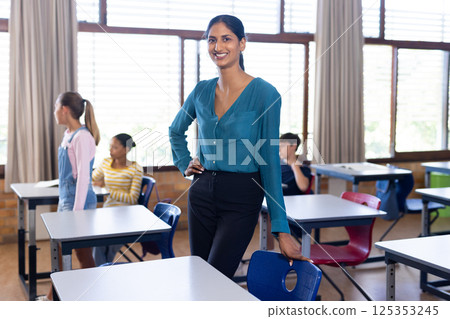 In school, Indian female teacher standing confidently in classroom with students in background In school, Indian female teacher standing confidently in classroom with students in background 125353245