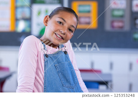 Smiling girl in overalls posing confidently in classroom at school 125353248