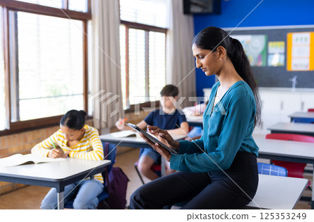 In school, Indian female teacher using tablet while students studying in classroom, copy space 125353249