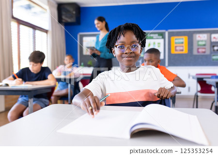 In school, student writing in notebook while classmates studying in classroom 125353254
