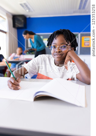 In school, boy writing in notebook while sitting at desk in classroom 125353258