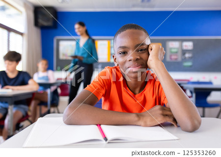 In school, boy sitting at desk with open notebook, smiling at camera In school, boy sitting at desk with open notebook, smiling at camera 125353260