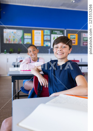 Smiling students sitting at desks in classroom, engaging in school activities 125353266