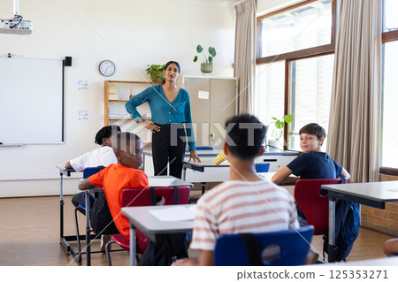 Indian female teacher standing in classroom, engaging with students during school lesson 125353271