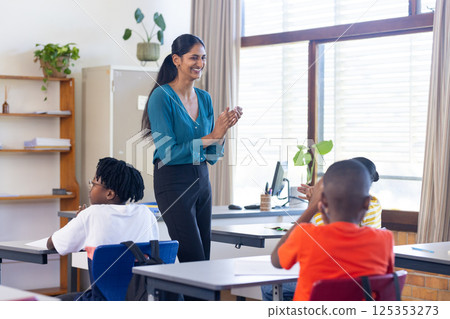 Indian female teacher clapping hands while students sitting at desks in school classroom Indian female teacher clapping hands while students sitting at desks in school classroom 125353273