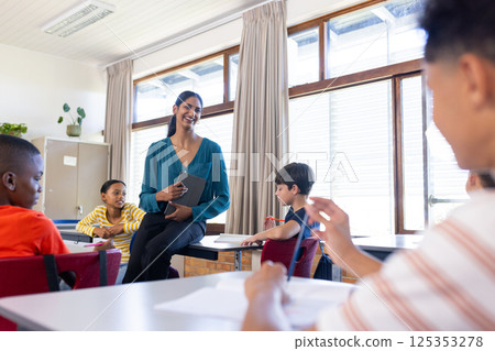 In school, Indian female teacher holding tablet and engaging with students in classroom In school, Indian female teacher holding tablet and engaging with students in classroom 125353278