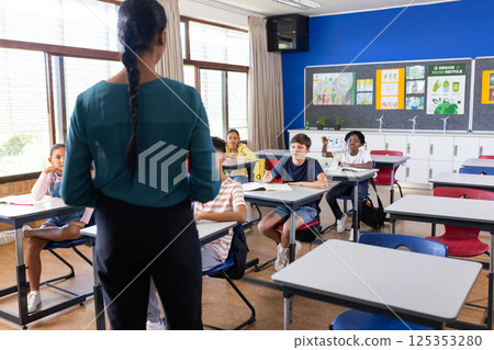Standing in classroom, indian female teacher instructing while students at desks listening Standing in classroom, indian female teacher instructing while students at desks listening 125353280
