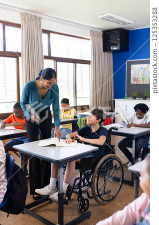 In school, Indian female teacher assisting student in wheelchair with classroom assignment In school, Indian female teacher assisting student in wheelchair with classroom assignment 125353288