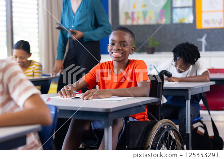 In school, boy in wheelchair smiling and writing at desk in classroom In school, boy in wheelchair smiling and writing at desk in classroom 125353291