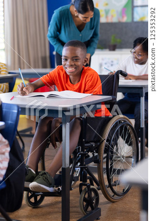 In school, boy in wheelchair writing in notebook, smiling in classroom In school, boy in wheelchair writing in notebook, smiling in classroom 125353292