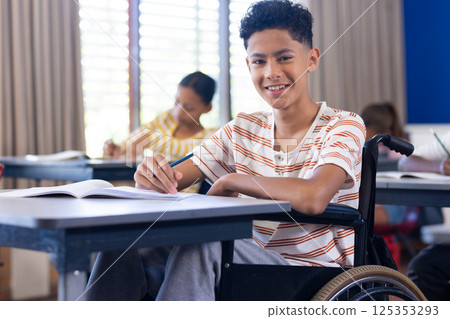 In school, boy in wheelchair writing in notebook, smiling in classroom In school, boy in wheelchair writing in notebook, smiling in classroom 125353293