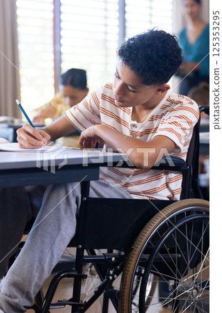 In school, boy in wheelchair writing in notebook, concentrating on task 125353295