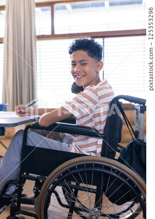 In school, boy in wheelchair smiling and writing in notebook in classroom In school, boy in wheelchair smiling and writing in notebook in classroom 125353296