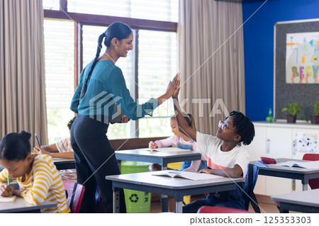 Indian female teacher giving high-five to student in classroom, encouraging learning in school 125353303