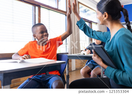In school, Indian female teacher high-fiving student while holding tablet in classroom In school, Indian female teacher high-fiving student while holding tablet in classroom 125353304
