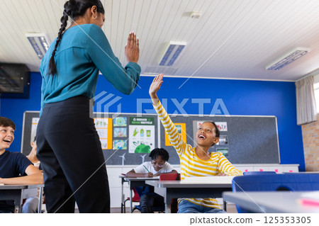 In school, Indian female teacher giving high-five to excited student in classroom, copy space 125353305