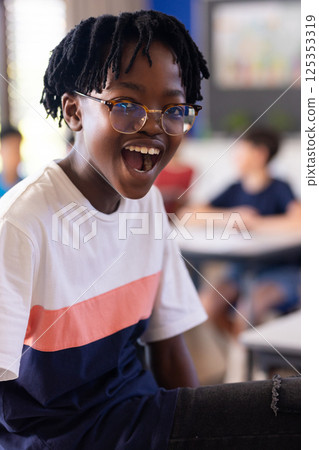 In school, excited student wearing glasses smiling in classroom with classmates In school, excited student wearing glasses smiling in classroom with classmates 125353319