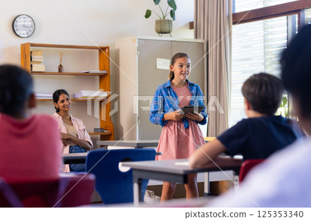 In school, girl presenting with tablet in classroom, engaging with students In school, girl presenting with tablet in classroom, engaging with students 125353340