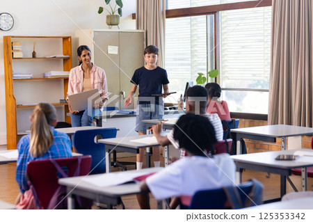 In school, Indian female teacher and student presenting with laptop in classroom to peers 125353342