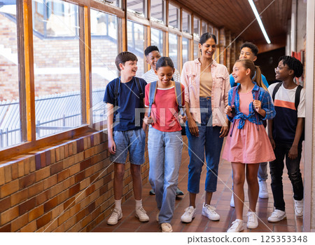 Walking in school hallway, Indian female teacher and students smiling and talking together 125353348