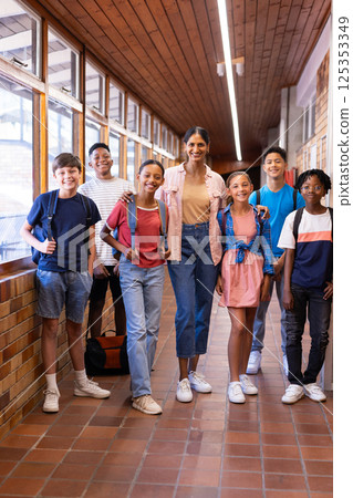 Indian female teacher standing with group of students in school hallway, all smiling 125353349