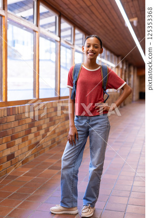 Smiling student with backpack standing in school hallway, posing confidently Smiling student with backpack standing in school hallway, posing confidently 125353368