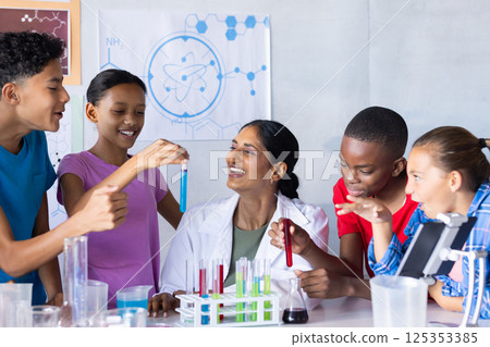 In school, students conducting science experiment with Indian female teacher, holding test tubes 125353385