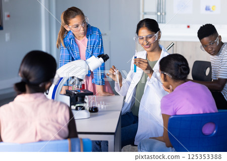 Indian female teacher demonstrating experiment with microscope and test tube, students in school 125353388