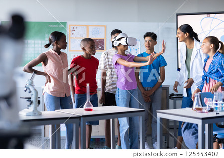 In school, students using VR headset in science classroom with Indian female teacher observing 125353402