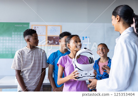 In school, students interacting with Indian female teacher while holding VR headset in classroom 125353404