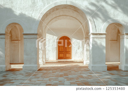 White arched corridor with terracotta tiles and large wooden door 125353480