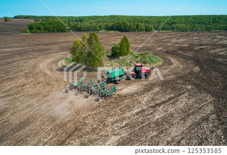 Tractor cultivating a field in springtime across an expansive landscape with clear skies 125353585