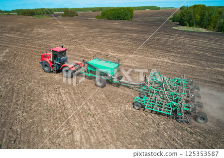 A red tractor is actively tilling a large, flat agricultural field A red tractor is actively tilling a large, flat agricultural field 125353587