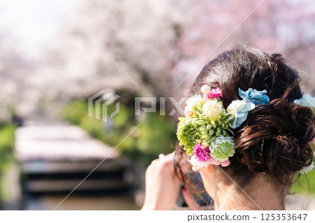 A beautiful view of Kawagoe: A middle-aged woman in a kimono taking a photo of a flower raft with her smartphone 125353647