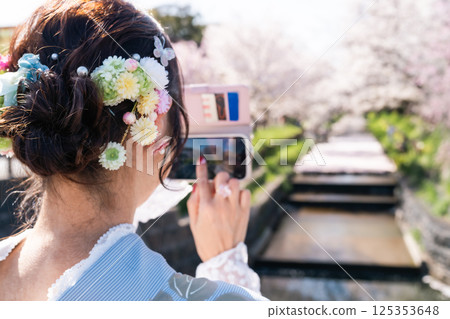 A beautiful view of Kawagoe: A middle-aged woman in a kimono taking a photo of a flower raft with her smartphone 125353648