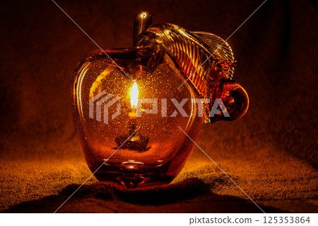 Apple from glass through which you can see a candle 125353864