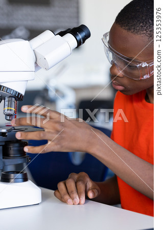 Using microscope, student conducting scientific experiment in school laboratory 125353976