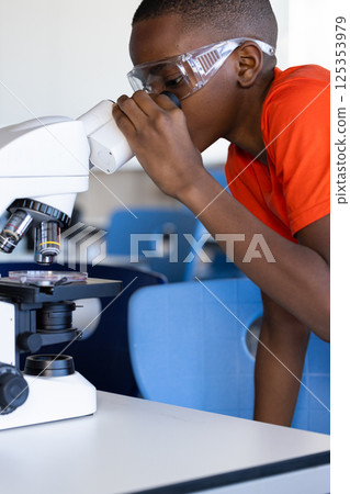 In school, boy using microscope and wearing safety goggles in science classroom 125353979