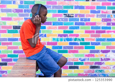 Listening to music with headphones, boy sitting against colorful brick wall, copy space Listening to music with headphones, boy sitting against colorful brick wall, copy space 125353990